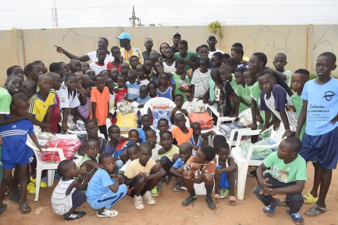 Distribution de fournitures scolaires dans une cour, entourée des enfants du quartier